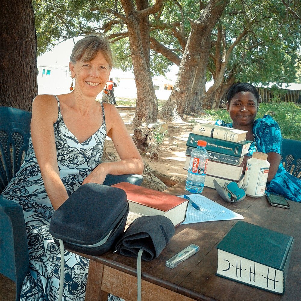 Miriam and Precious with homeopathy books under a tree waiting for patients.